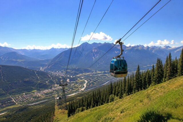 Summer gondola ride over a lush mountain valley with stunning alpine peaks, forests, and blue skies.