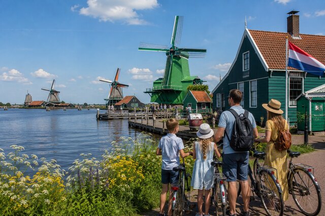 Family exploring a Dutch waterfront by bicycle with traditional houses, canals, and windmills in the Netherlands.