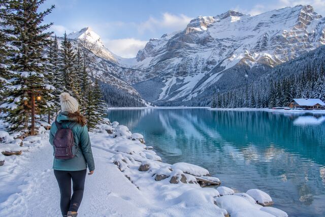 Non-skier enjoying a peaceful winter walk beside a turquoise lake in Banff, surrounded by snow-covered mountains and evergreen trees.